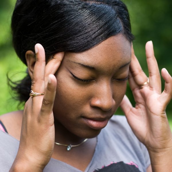 A young woman holding her head, feeling the intense pain of a splitting migraine