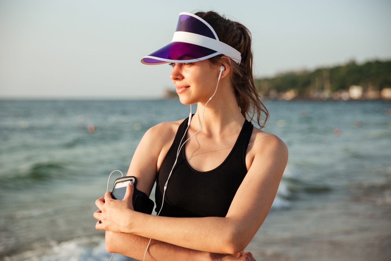 Young fitness runner woman resting on beach listening to music with phone case sport armband strap