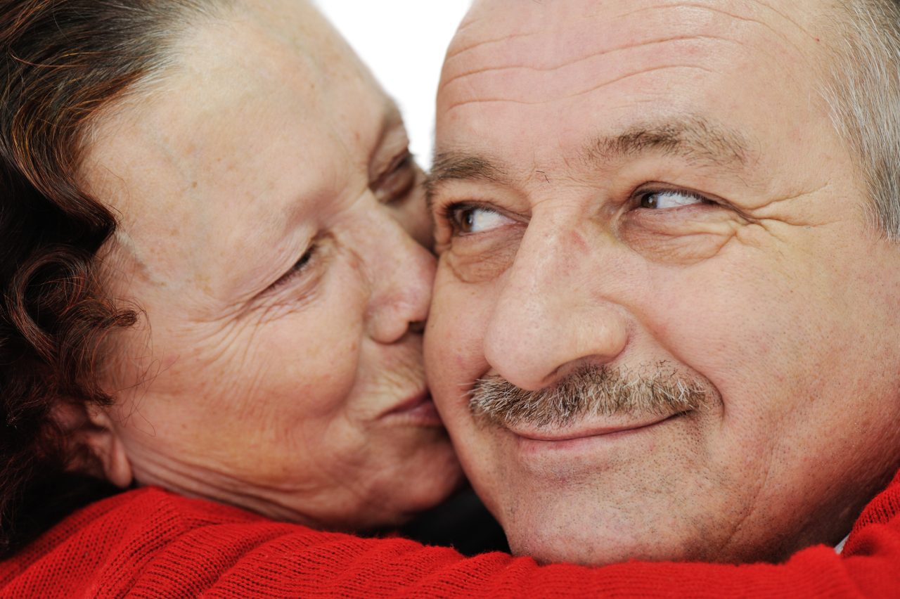 Closeup image of elderly woman kissing in a cheek her husband
