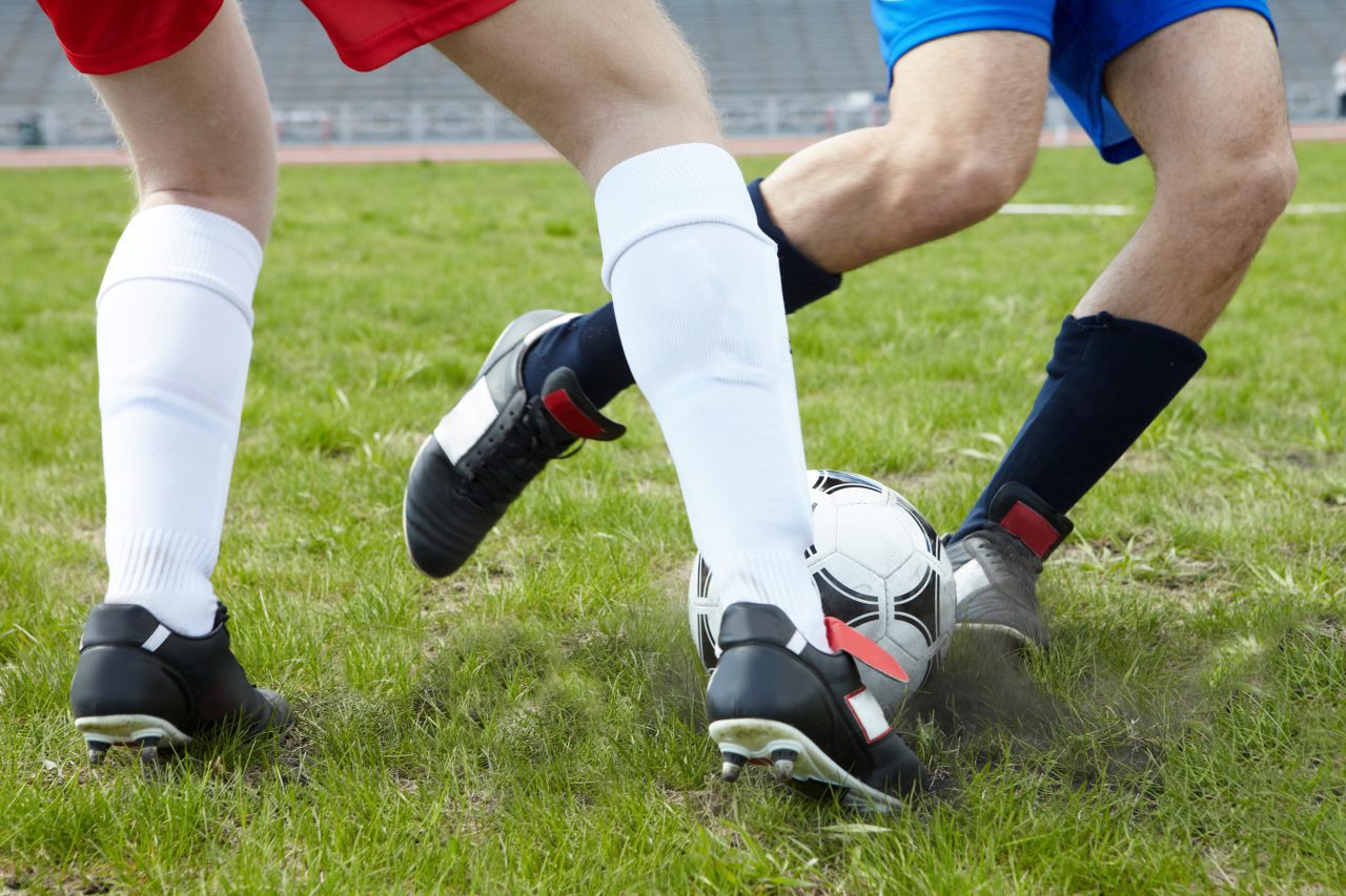 Image of footballers legs kicking soccer ball on stadium