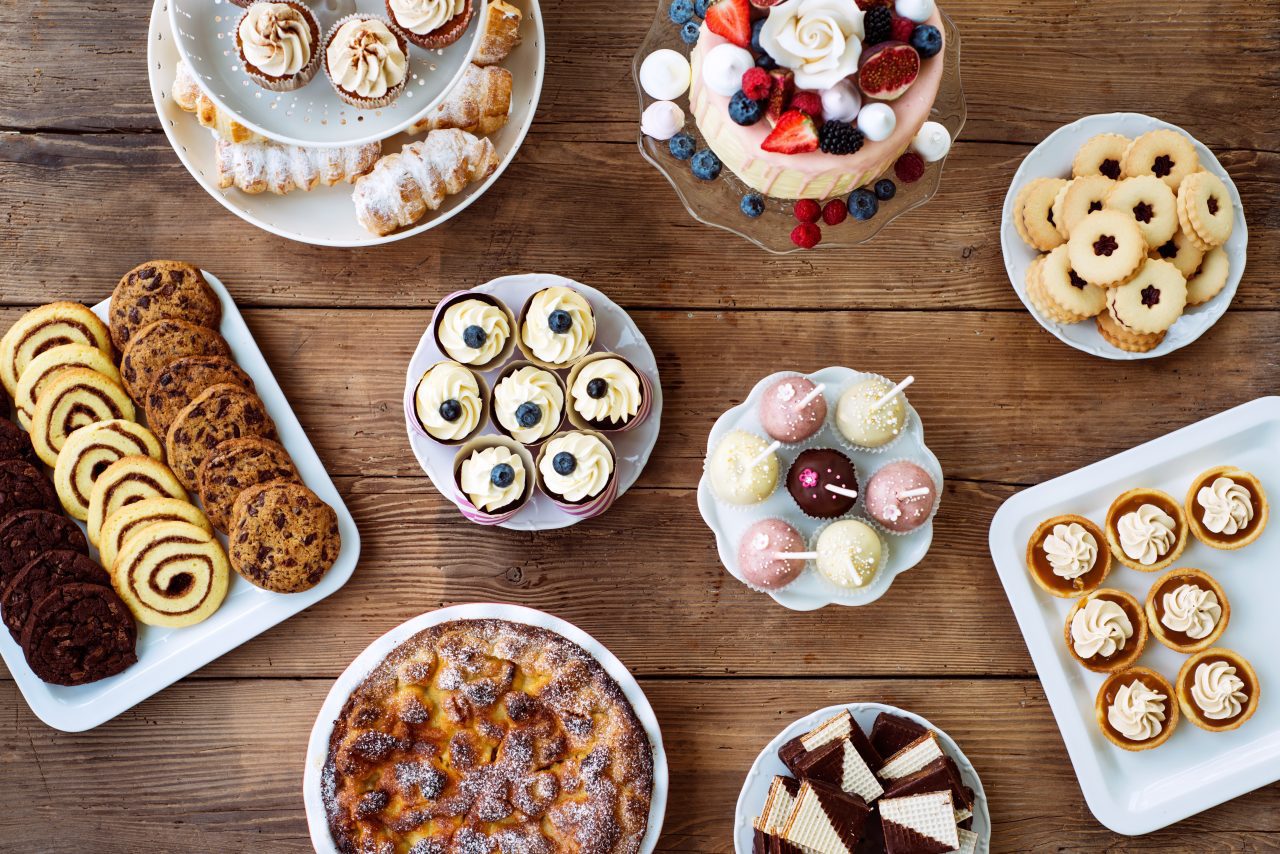 Table with cake, pie, cupcakes, cookies, tarts and cakepops. Studio shot on brown wooden background. Flat lay.